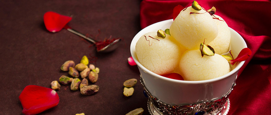 Rasgulla in a silver bowl with rose petals in brown background